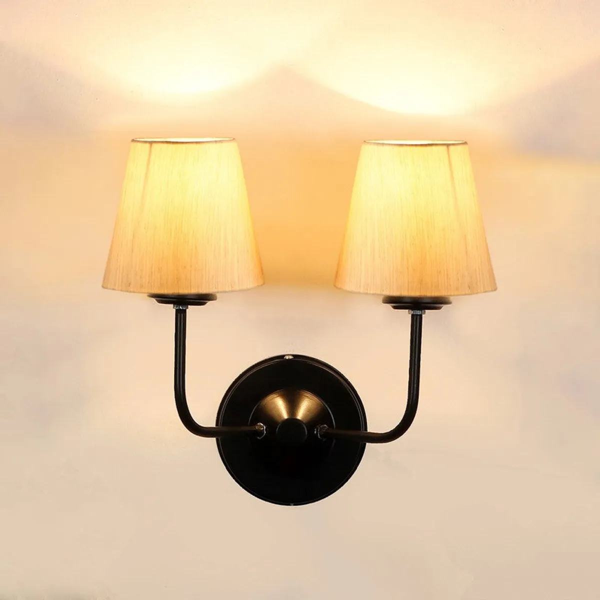 Front view of lit twin-shade beige wall lamp with black iron arms