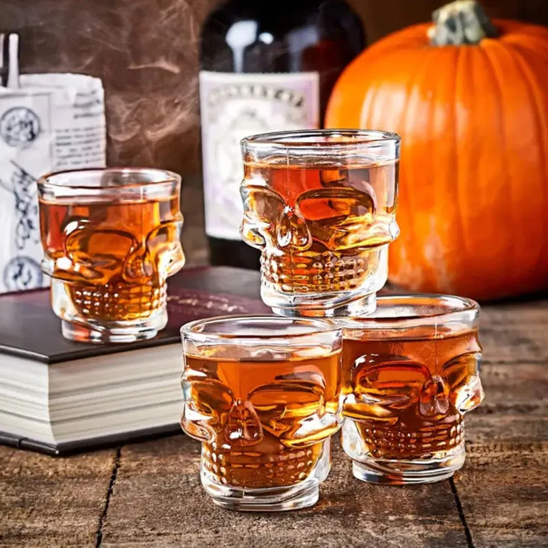 Clear skull-shaped shot glasses filled with amber drinks beside a pumpkin