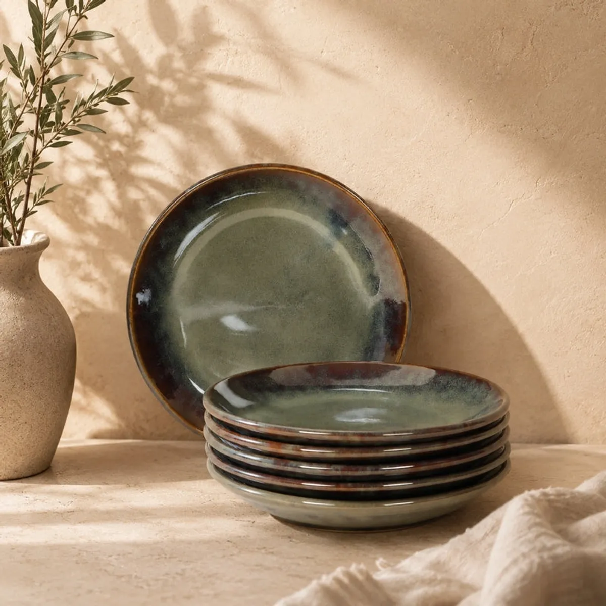 Olive green plate stack styled beside a ceramic vase and foliage