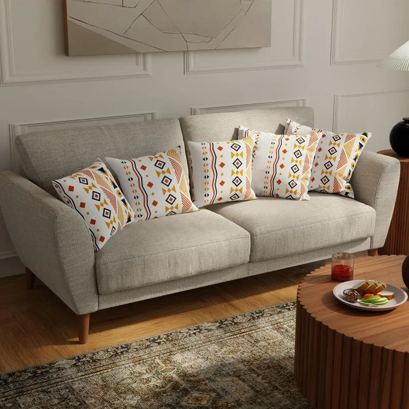 Five multicolour geometric cushion covers displayed on a beige sofa
