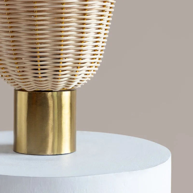 Close-up of the rattan shade meeting the gold metal base on a white pedestal