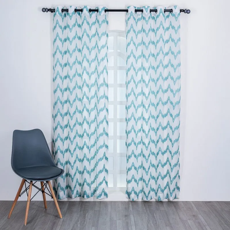 Blue and white abstract patterned sheer curtains framing a window in a bright room.