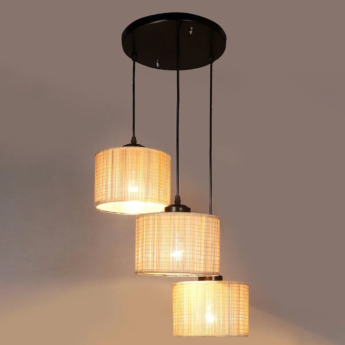 Three-light beige ceiling lamp switched on against a plain background