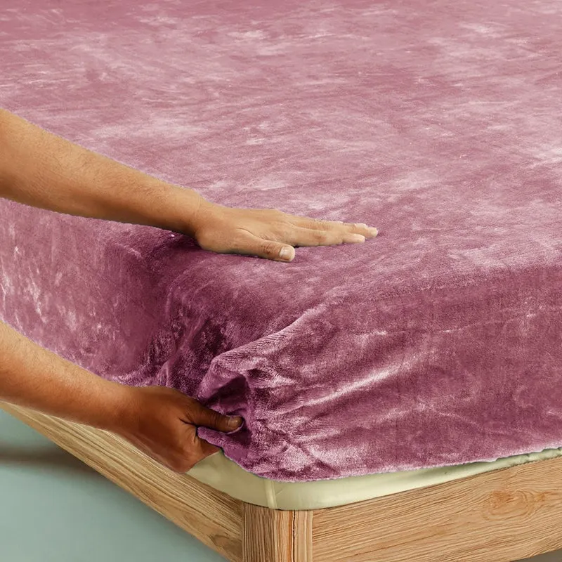 Pink velvet fitted bedsheet being placed over a mattress corner