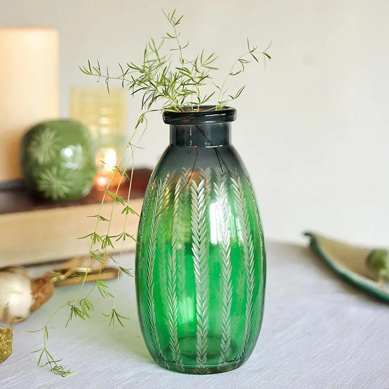 Green glass bottle vase with etched leaf pattern and dark rim on a tabletop
