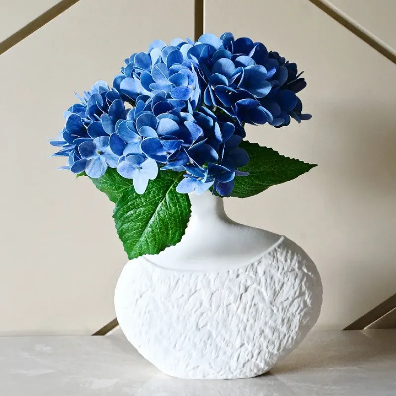 White textured vase filled with blue hydrangeas on a stone surface.