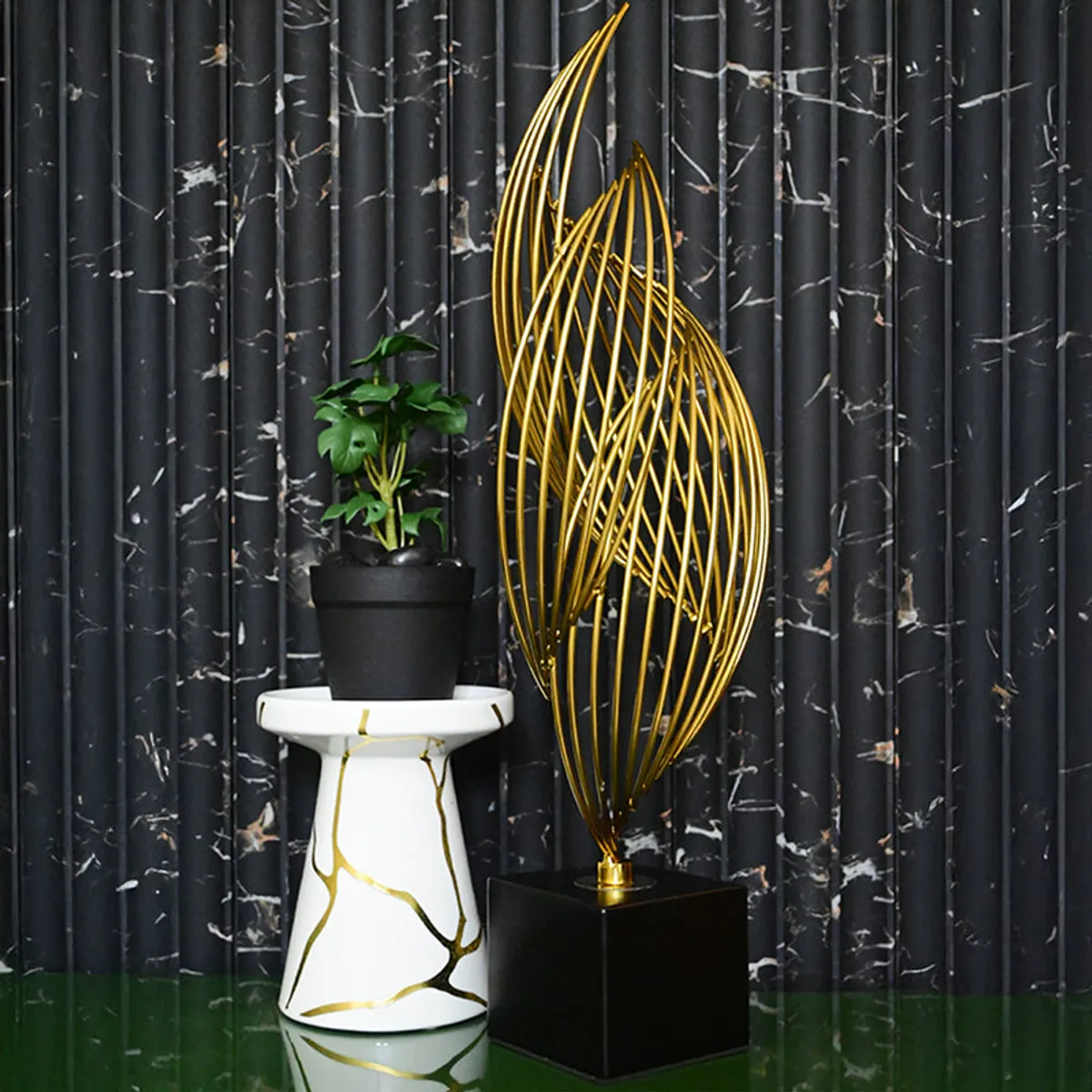 Gold abstract metal showpiece on a black base styled beside a plant stand