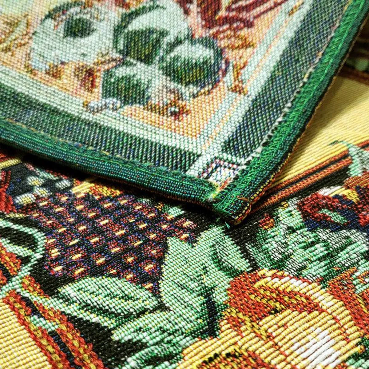 Close-up of woven placemat corner showing multicolour floral and fruit border