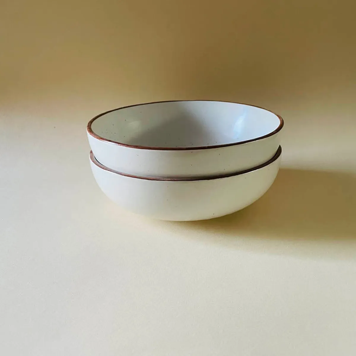 Two matching beige bowls with brown rims stacked one above the other.