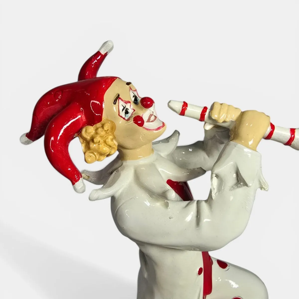 Upper-body close-up of clown figurine holding a striped pipe