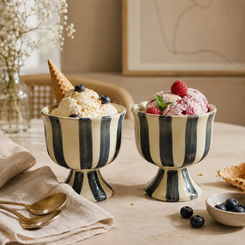 Two striped pedestal ice cream cups filled with scoops of ice cream on a dining table