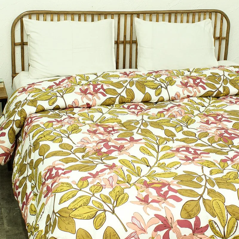 Floral comforter draped over a bed with leafy pink and olive motifs
