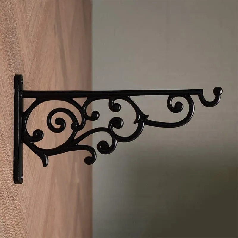 Black vintage wall bracket with ornate scrollwork mounted on a wooden wall.