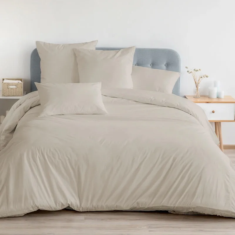 Beige fitted bedsheet and pillows styled on a bed with blue headboard