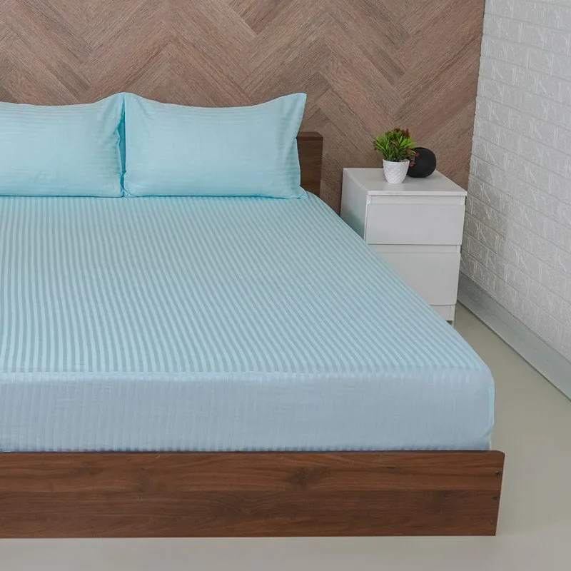 Close view of light blue striped fitted bedsheet on a bed with matching pillows