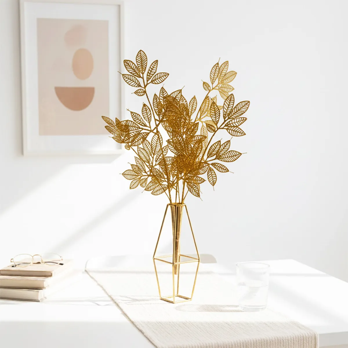 Golden leaf stems in a green glass vase beside books and a teacup