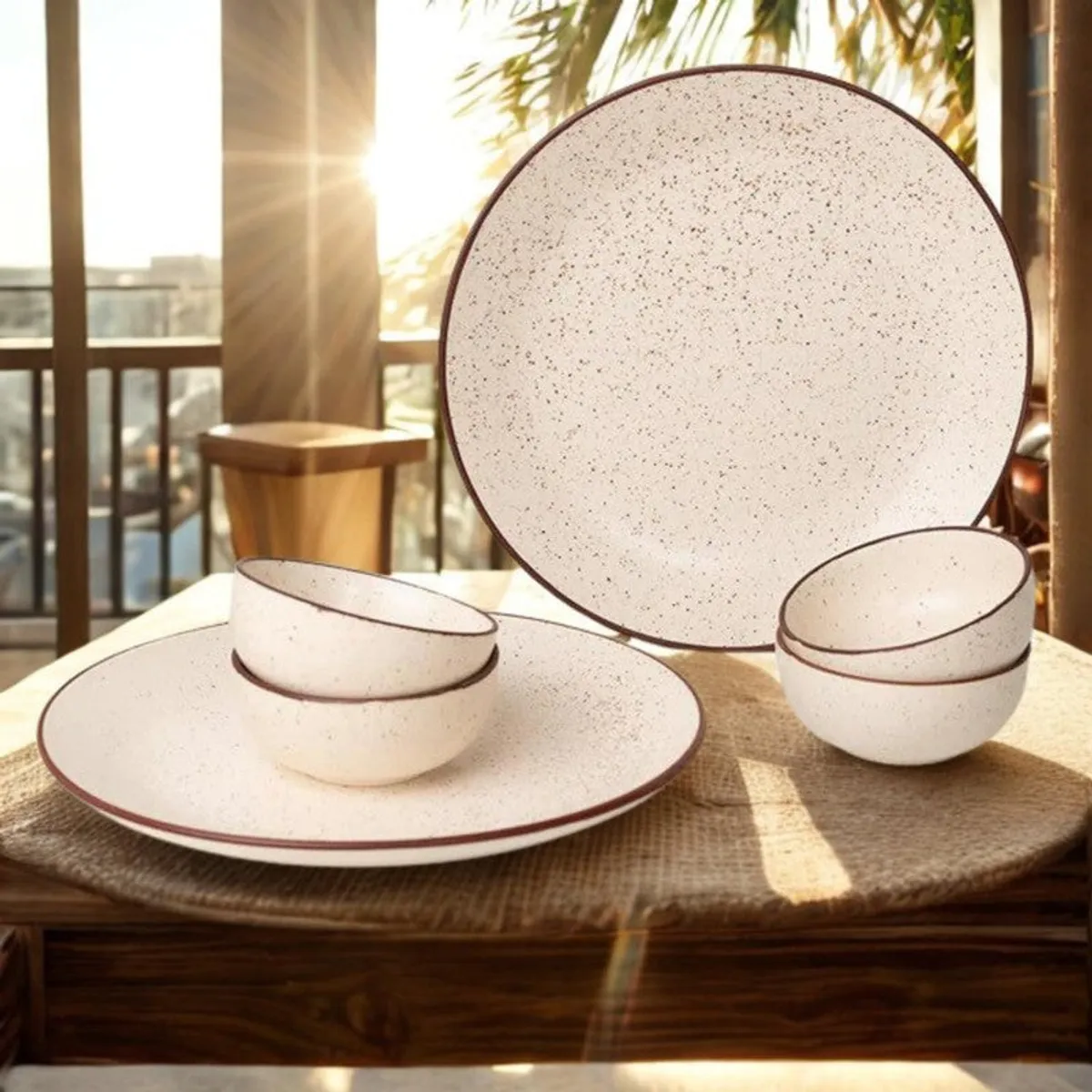 Beige speckled plates and bowls with brown rims displayed on a sunlit dining table.