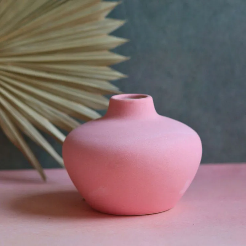Pink rounded ceramic vase with a narrow neck on a pink tabletop
