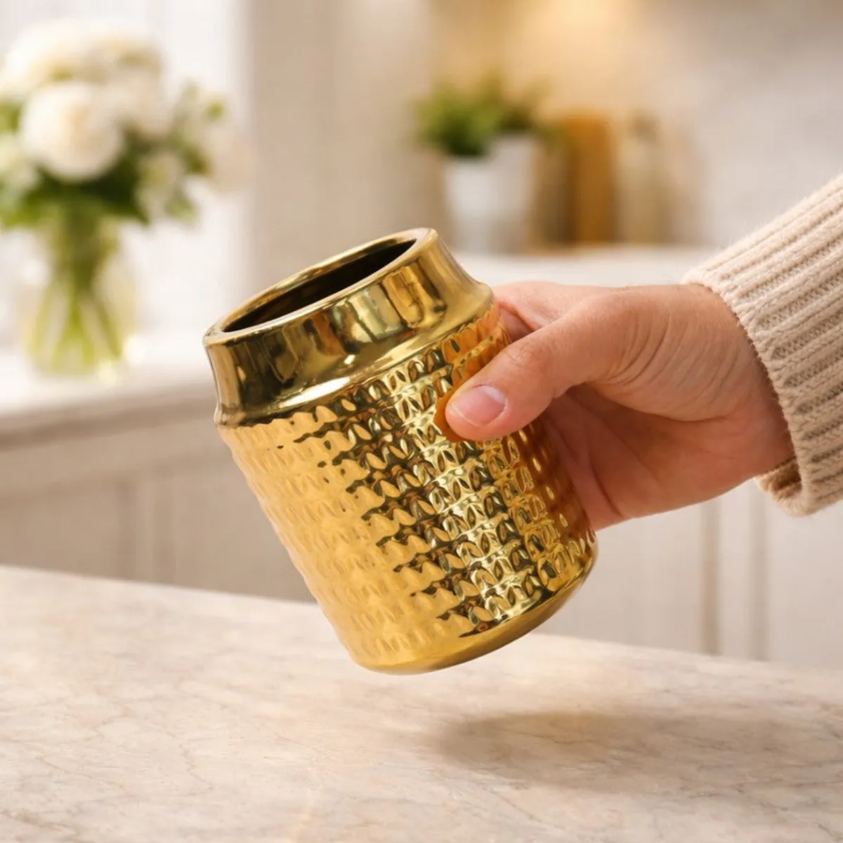 Hand holding a gold ribbed ceramic vase in a softly lit interior.