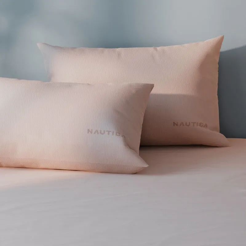 Close-up of pink bedding with matching branded pillow covers against a blue wall