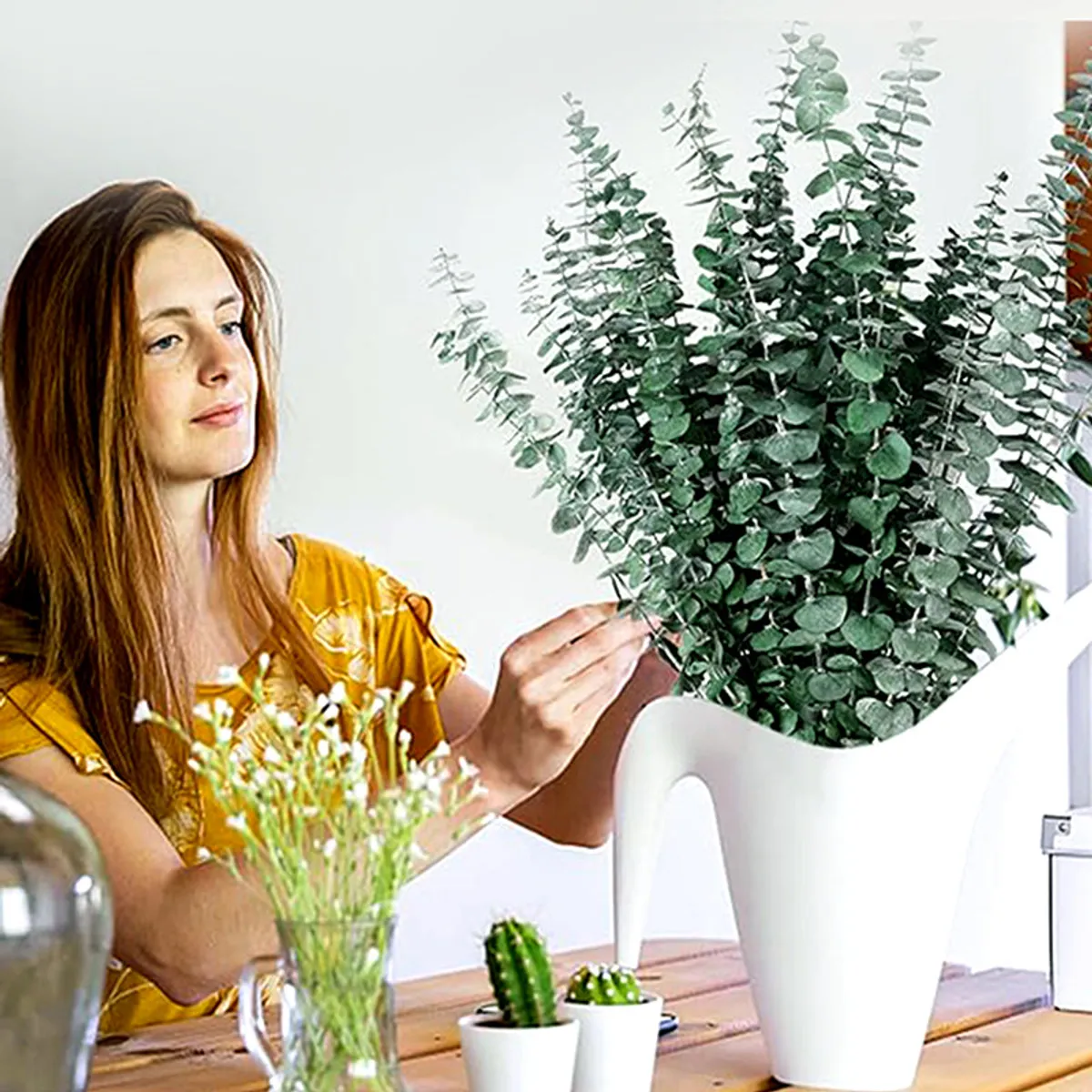 Woman arranging a large bunch of eucalyptus stems in a white planter