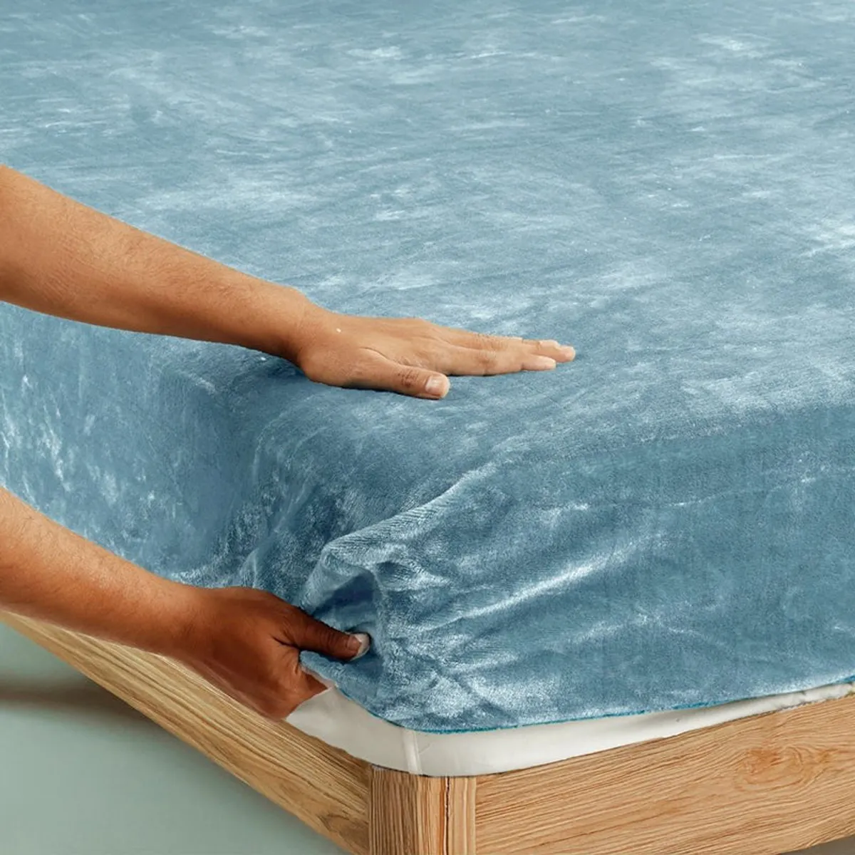 Sky blue velvet fitted bedsheet being stretched over a mattress corner