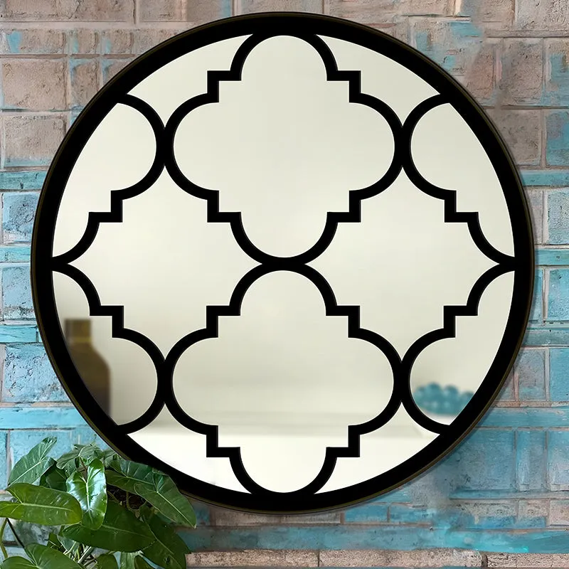 Round black decorative mirror with geometric pattern against a brick wall