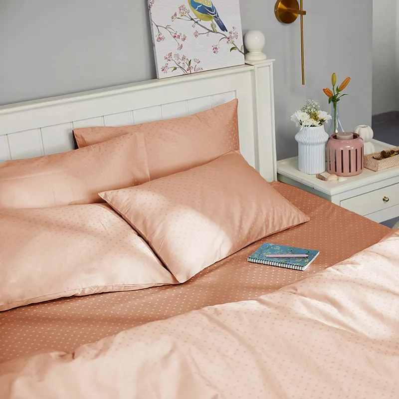 Peach dotted bedding styled with pillows in a bright bedroom