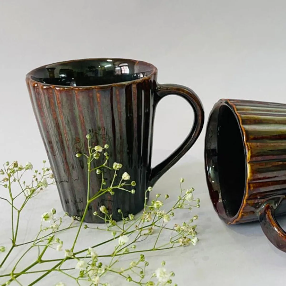 Upright glossy brown mug beside a second ribbed mug on its side