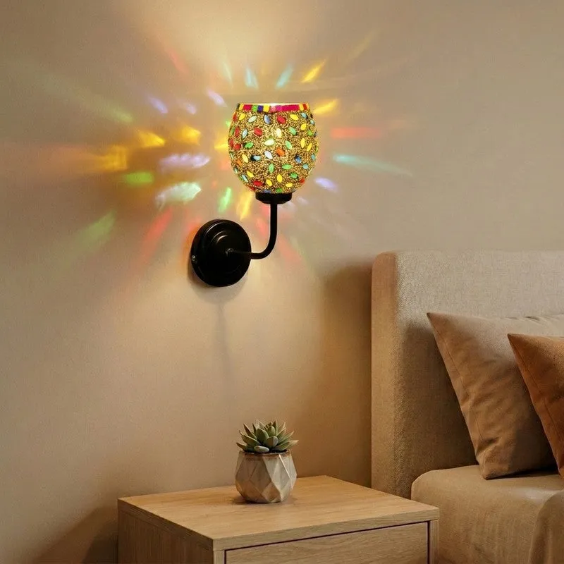 Multicolour mosaic glass wall lamp lit on a beige wall beside a bedside table