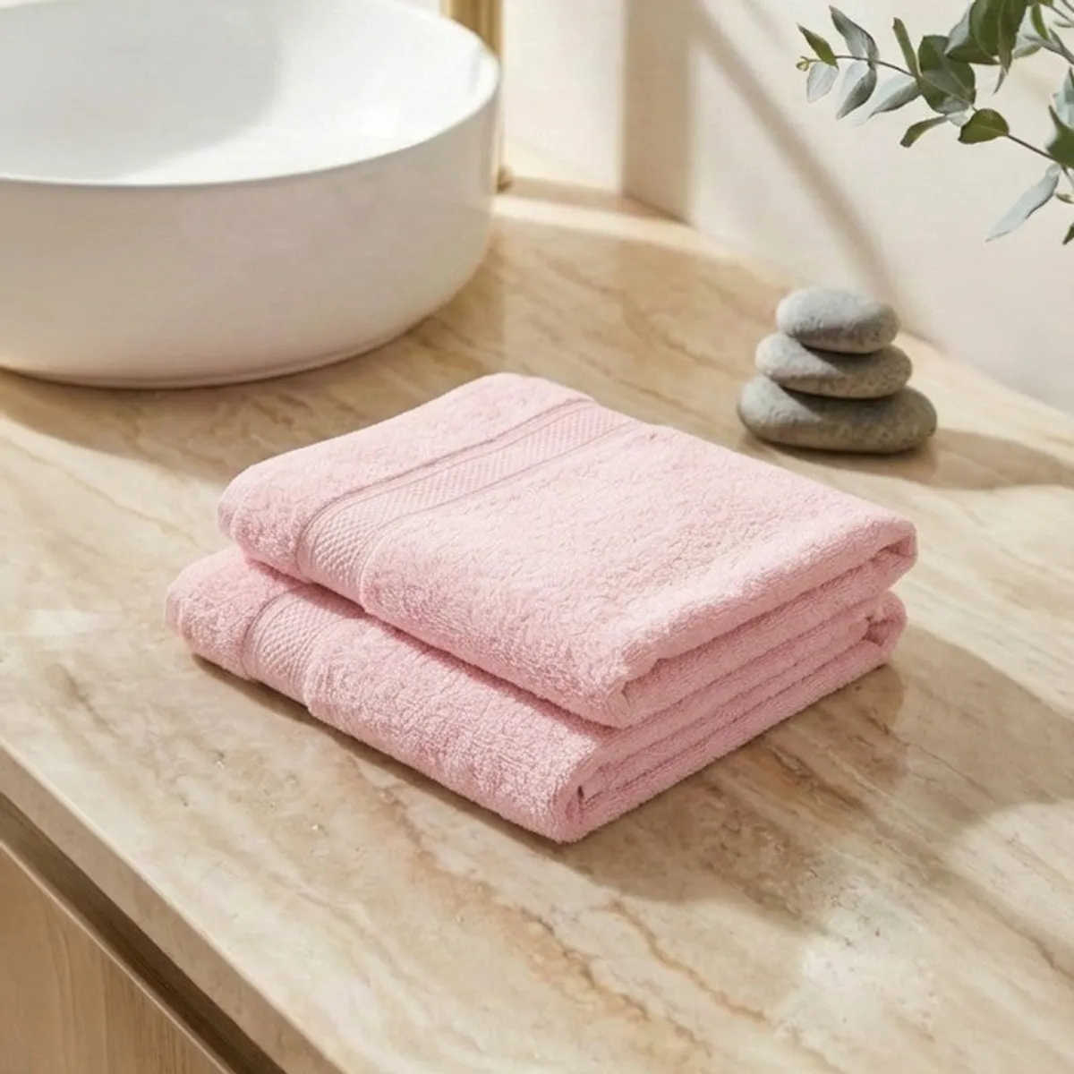Two folded light pink hand towels on a wooden bathroom counter