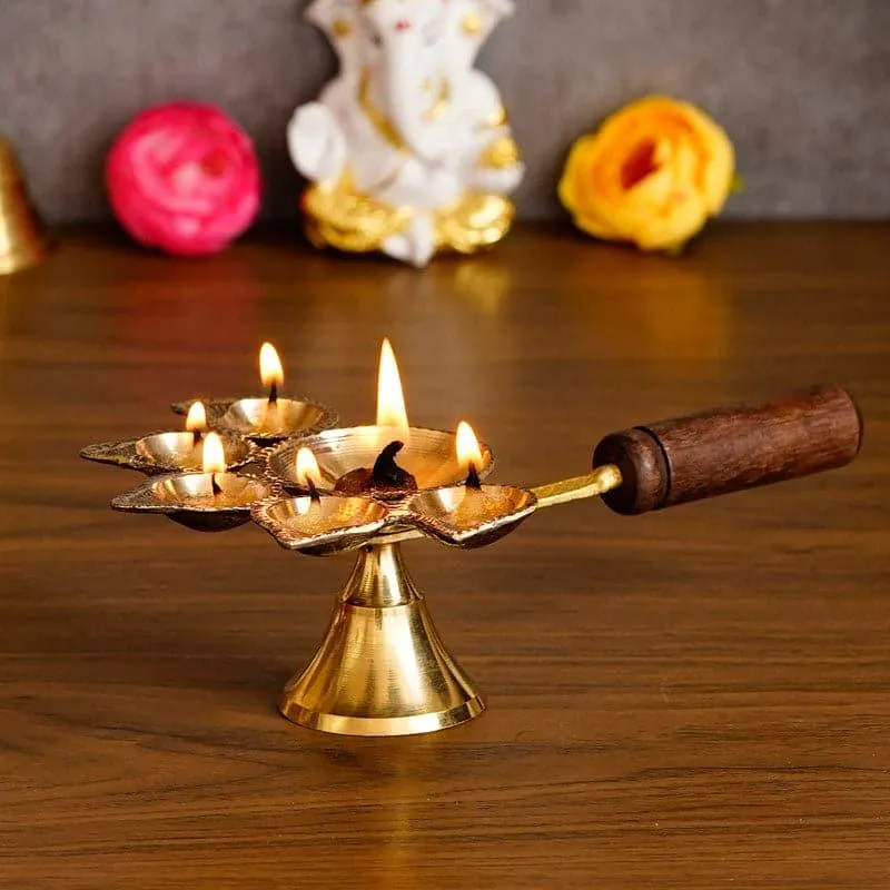 Lit gold-toned panchdeep diya with a brown wooden handle on a wooden surface