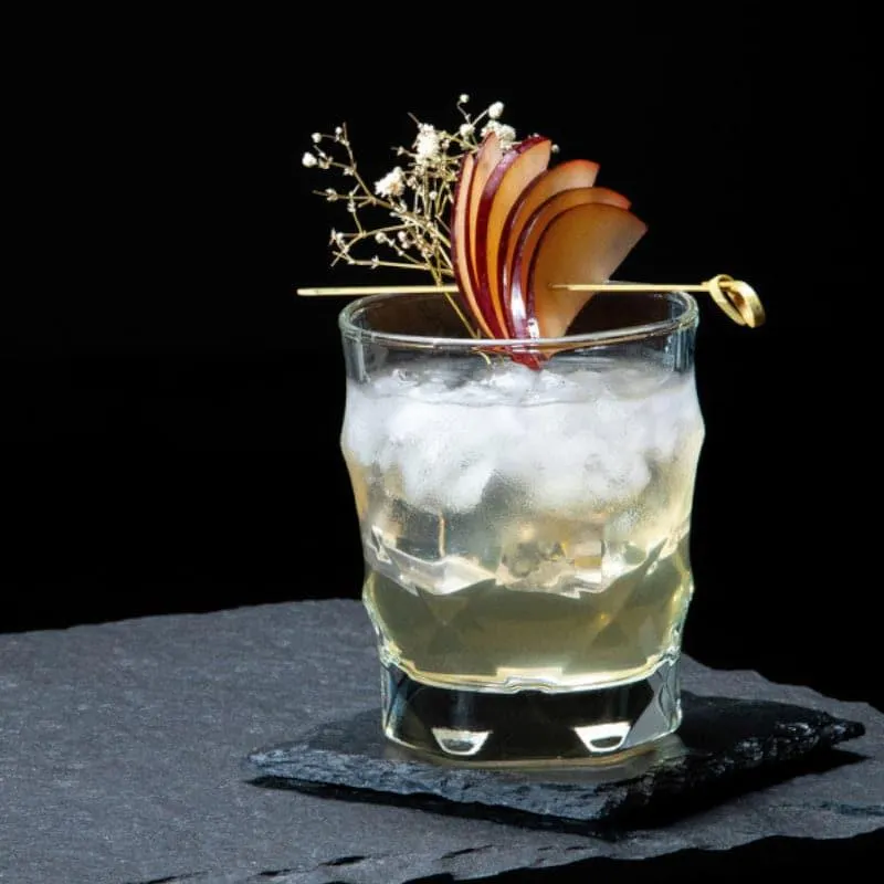 Single transparent faceted tumbler with iced drink and garnish on a dark surface