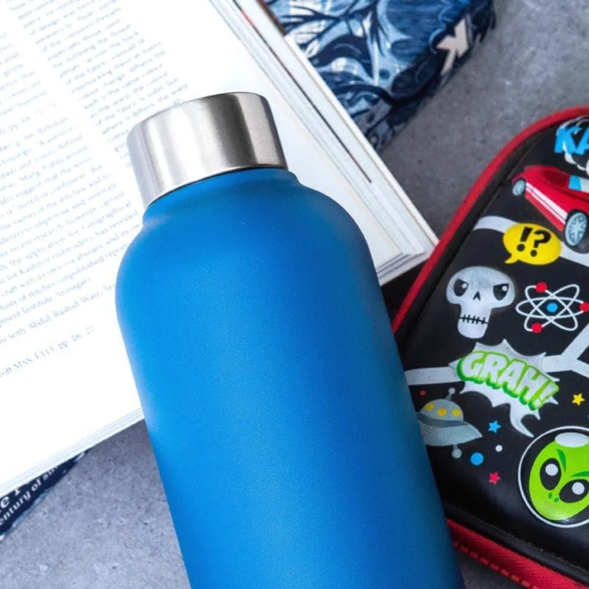 Close-up of the matte blue bottle and silver cap beside an open book.