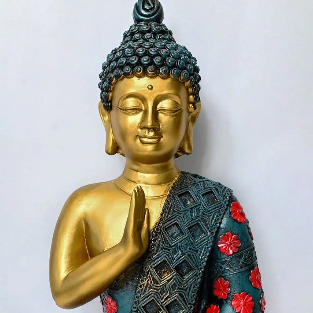 Close-up portrait of golden Buddha idol with textured teal drape and red accents