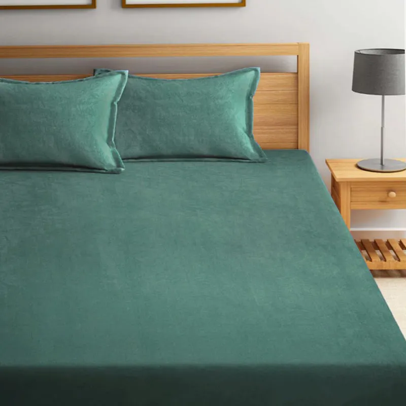 Close view of a dark green bedsheet on a wooden bed beside a lamp