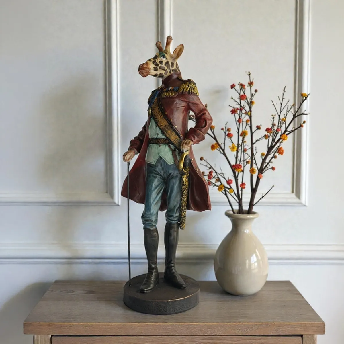 Animal-headed figurine on a wooden console beside a cream vase with flowering branches.