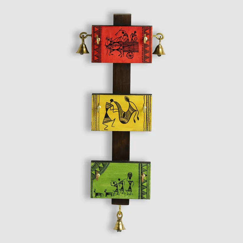 Front view of a multicolour wooden key hook with tribal figures, three panels and golden bells.