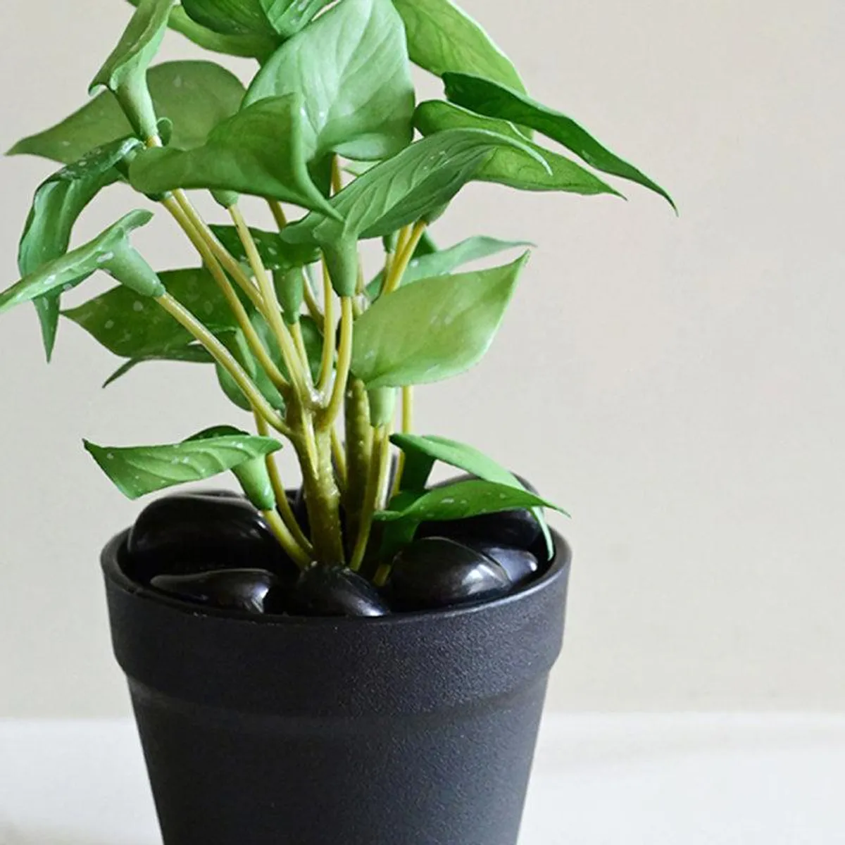 Close-up of green artificial pothos leaves and black pebbles in a pot