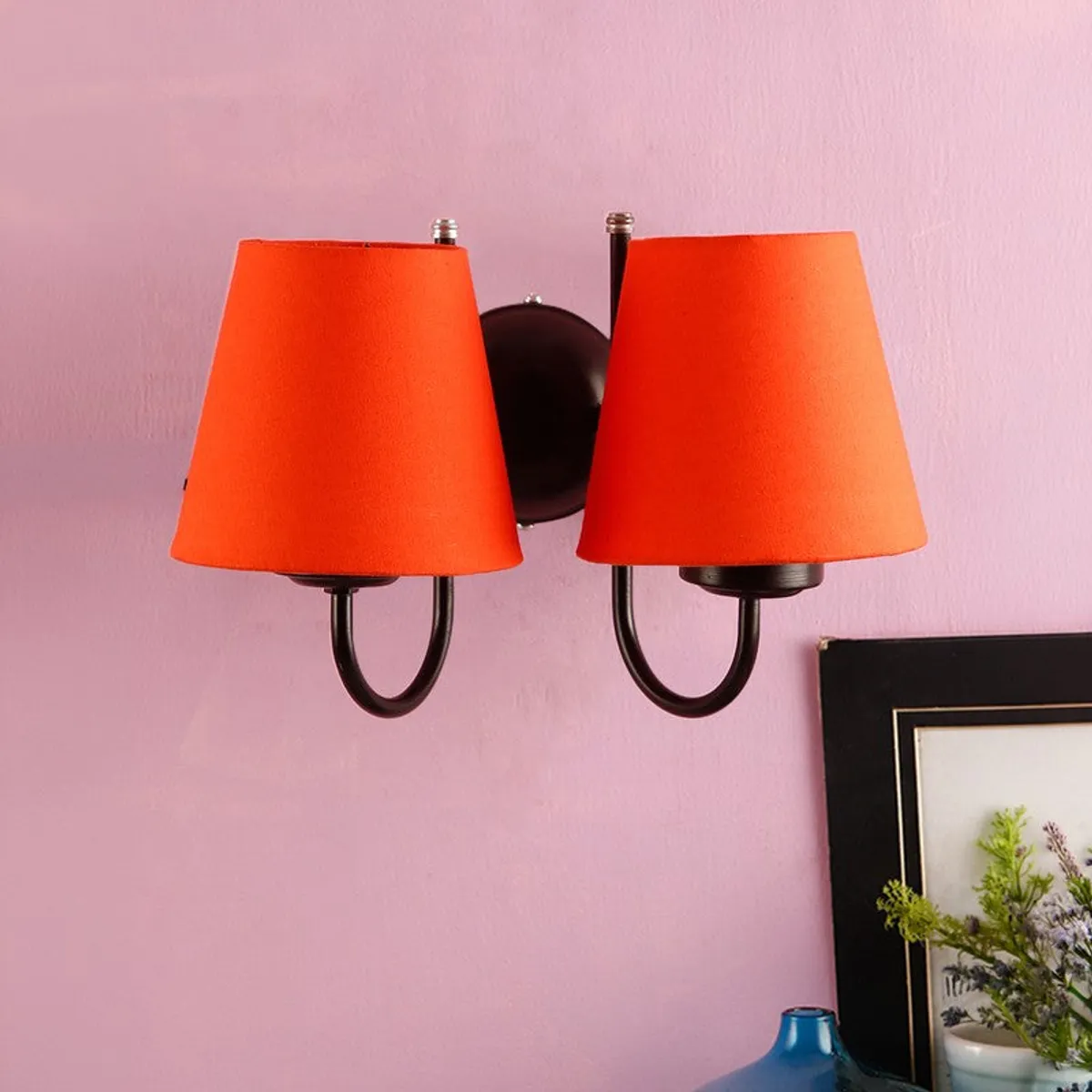 Orange double wall lamp with black iron base on a pink wall