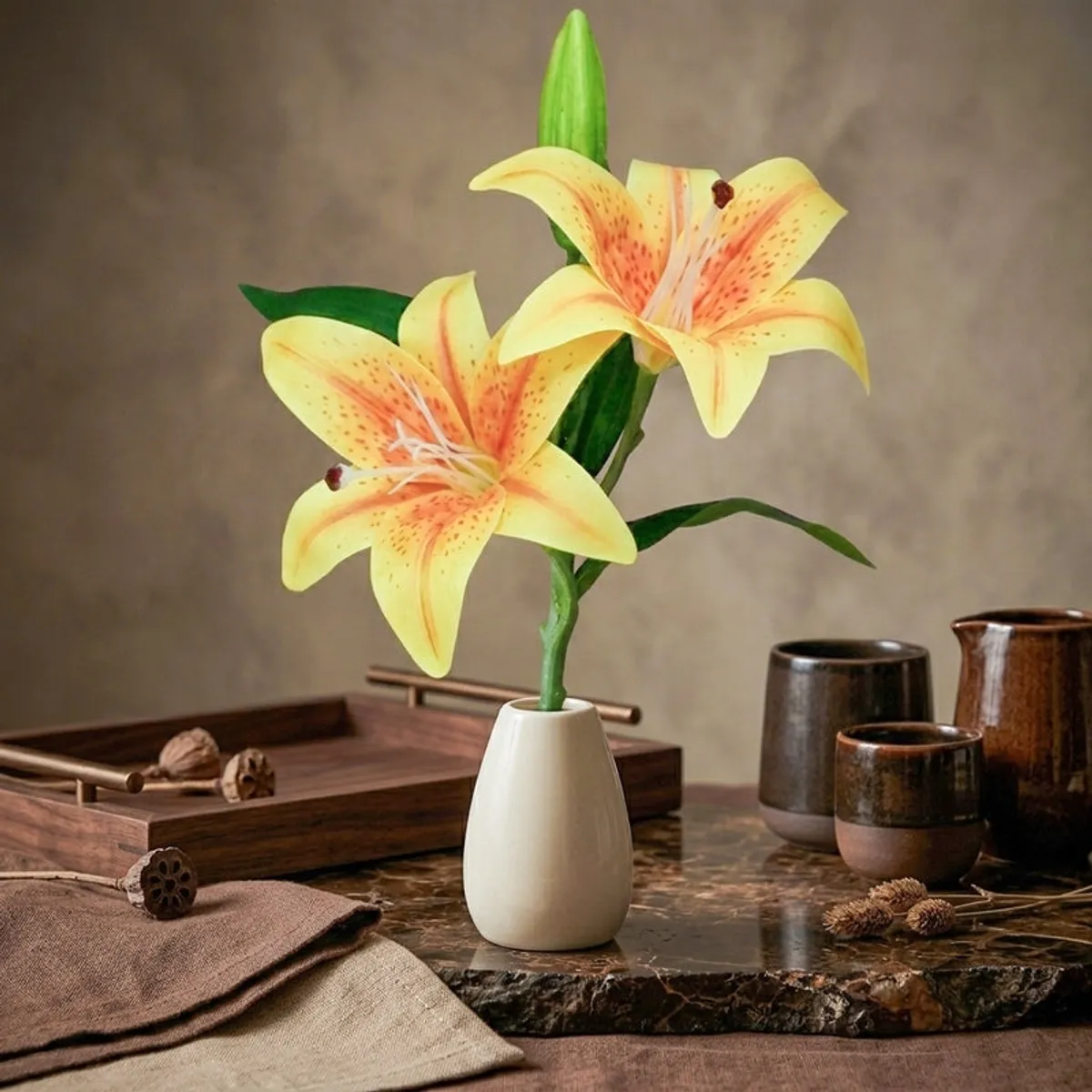 Yellow and orange artificial lily flower stick styled on a dark tabletop