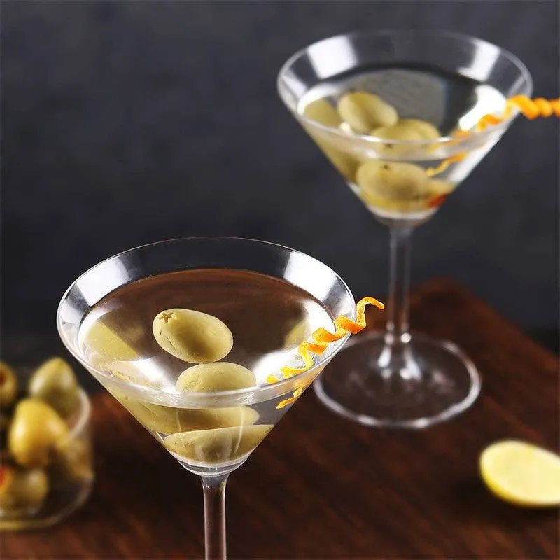 Two clear stemmed cocktail glasses with olives and citrus peel garnish