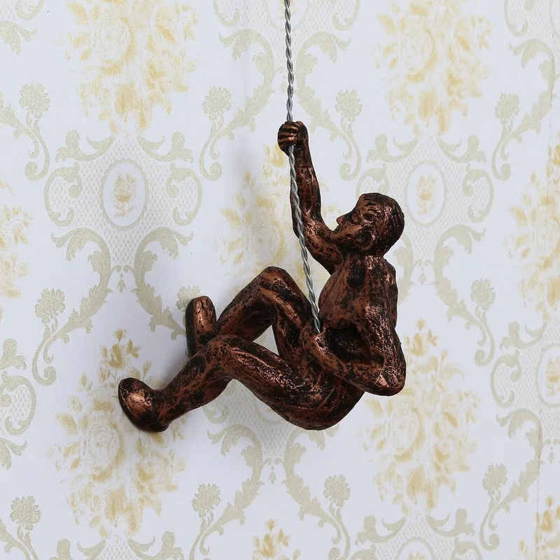 Bronze-toned climbing human figure wall accent against patterned wallpaper