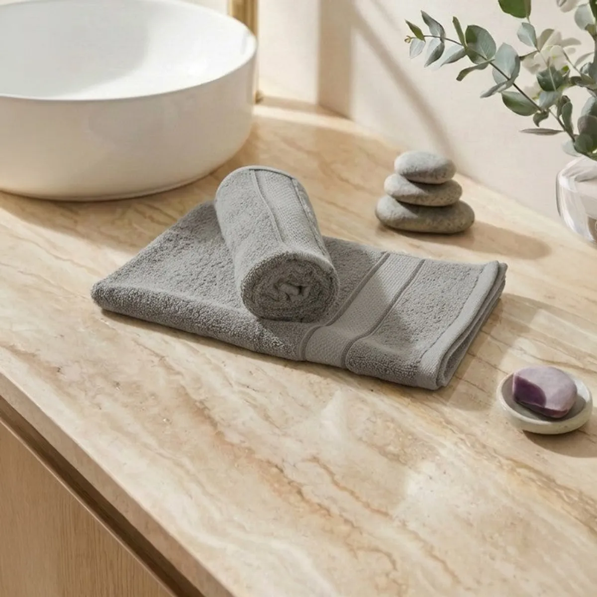Rolled and folded light grey hand towels on a stone bathroom counter