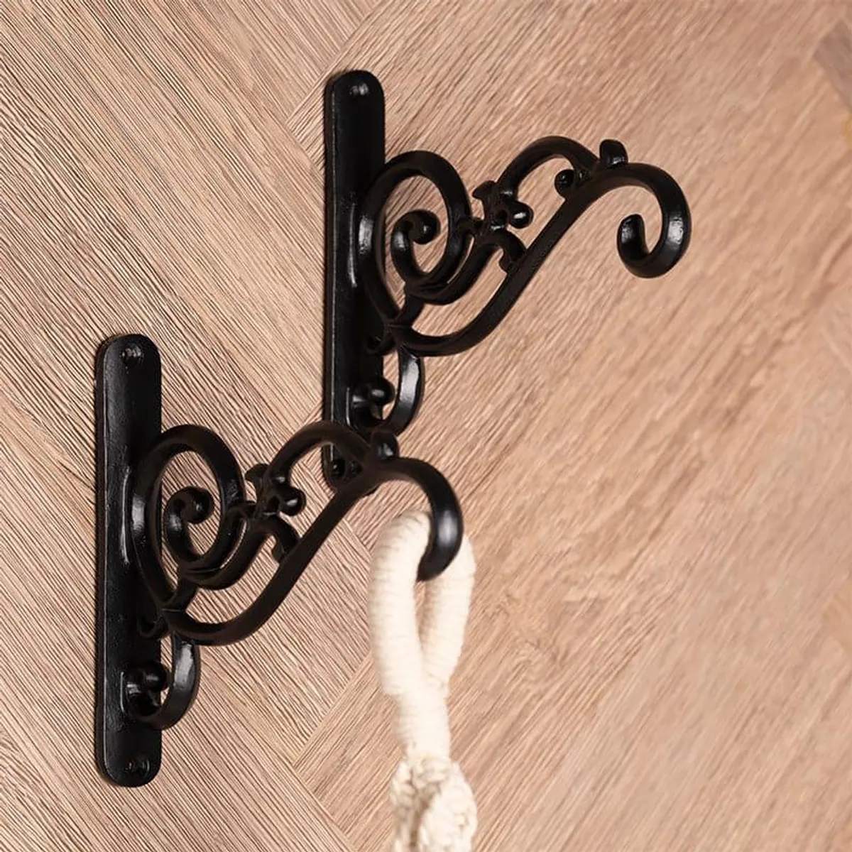 Two black ornate wall brackets mounted on a wall, with a light fabric hanging from one.