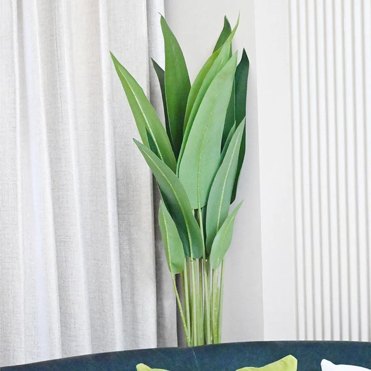 Tall artificial green plant beside curtains and a sofa