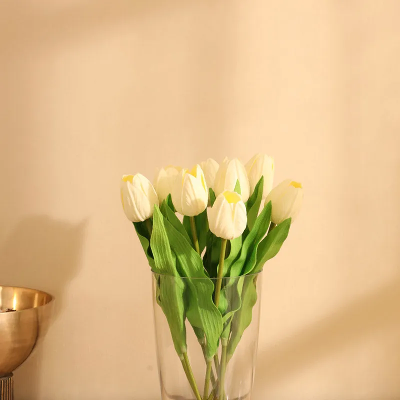 Close view of white artificial tulip blooms and green leaves in a vase