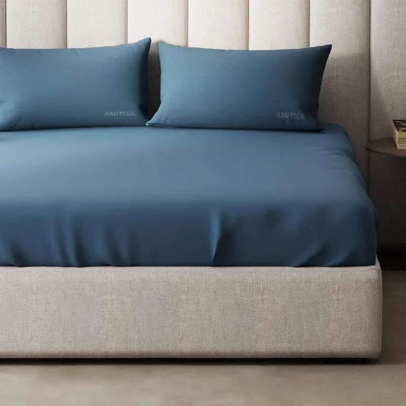 Close-up of blue flat bedsheet draped over the side of a bed