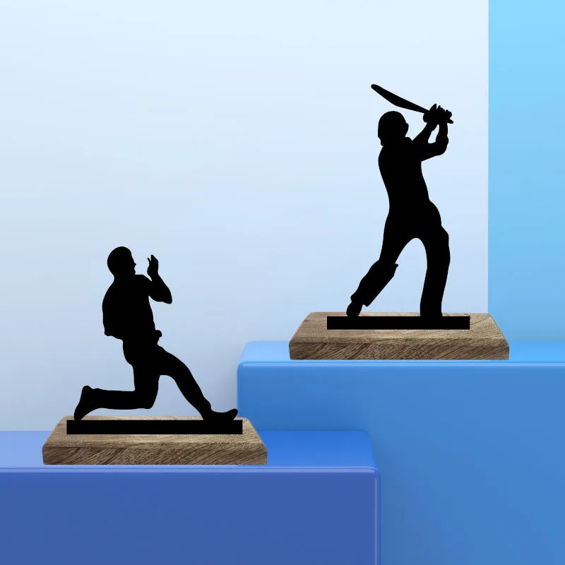 Two black cricket figurines on wooden bases displayed on blue plinths
