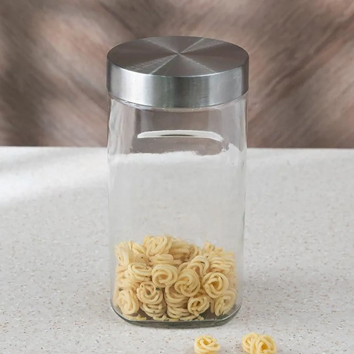 Clear cylindrical storage container with a silver lid and pasta inside.